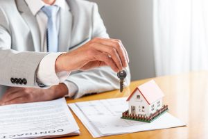 person-holding-house-keys-toy-model-house-desk (1)